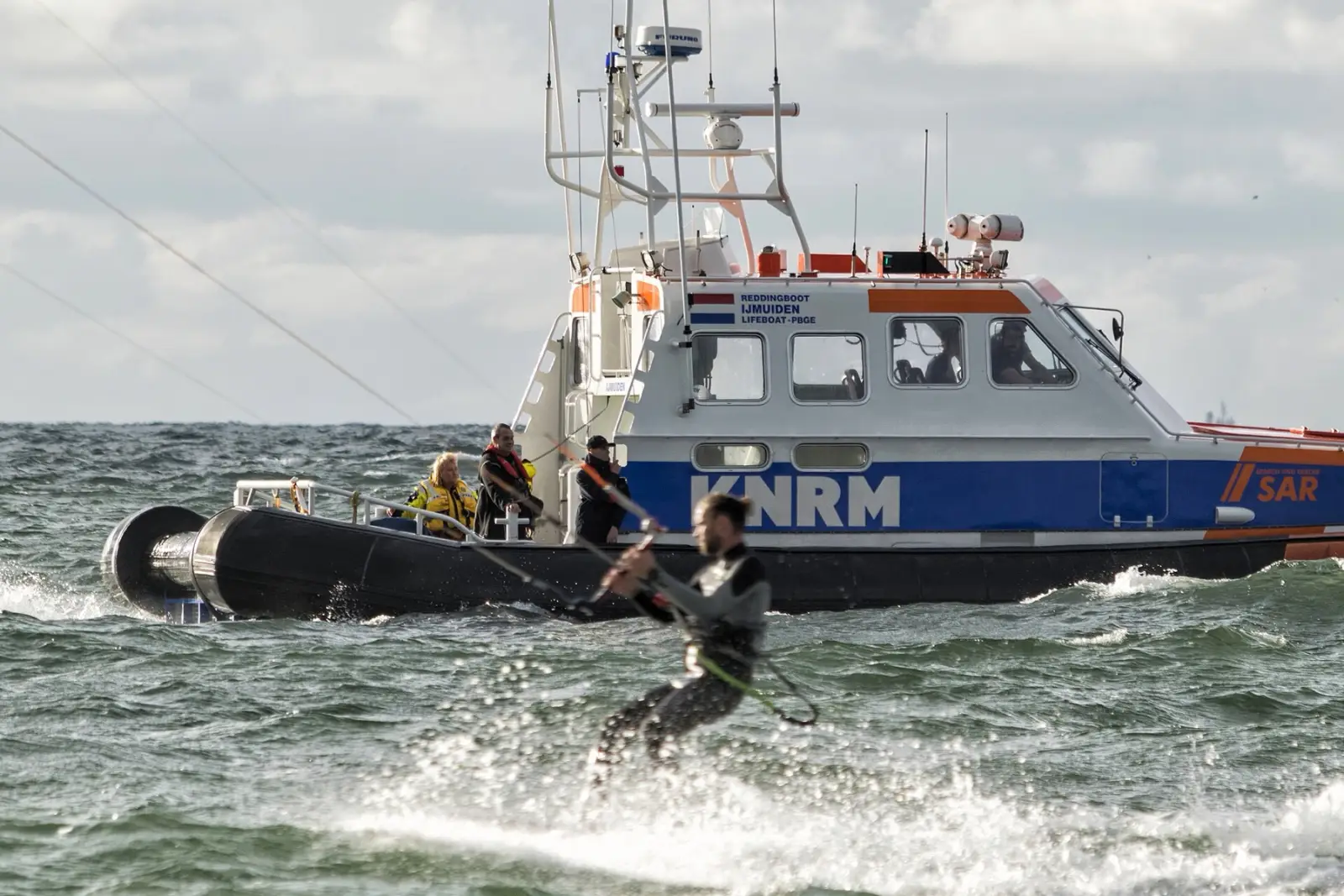 Een kitesurfer vaart vlak langs een reddingboot van de KNRM