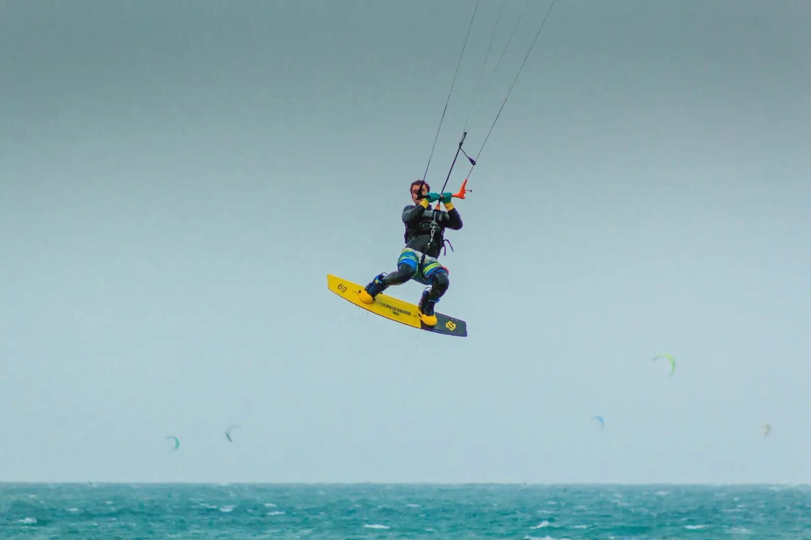 Een kitesurfer hoog in de lucht op een twintip boven een turquoise zee