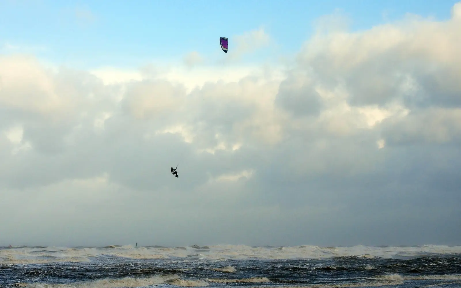 Een kiter hangt hoog boven een grauwe, woeste zee tijdens een storm