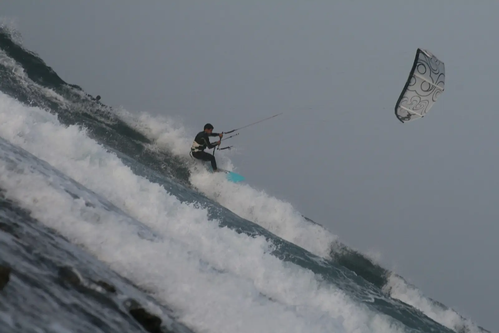 Een kiter op een surfboard zonder voetbanden snijdt door een brekende golf