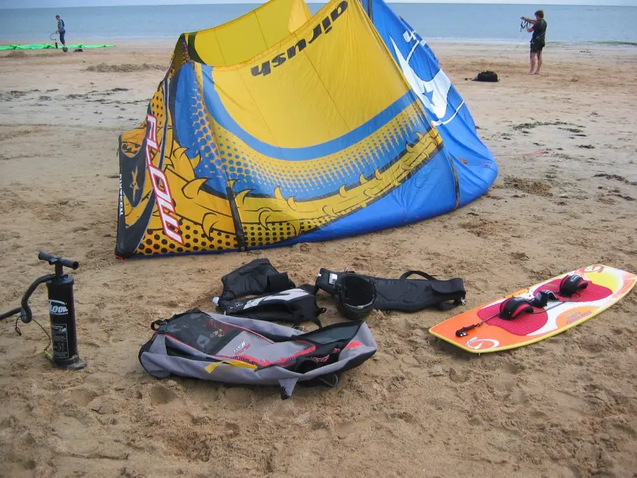 A kite, a pump, a harness and a twintip lying side by side on the beach