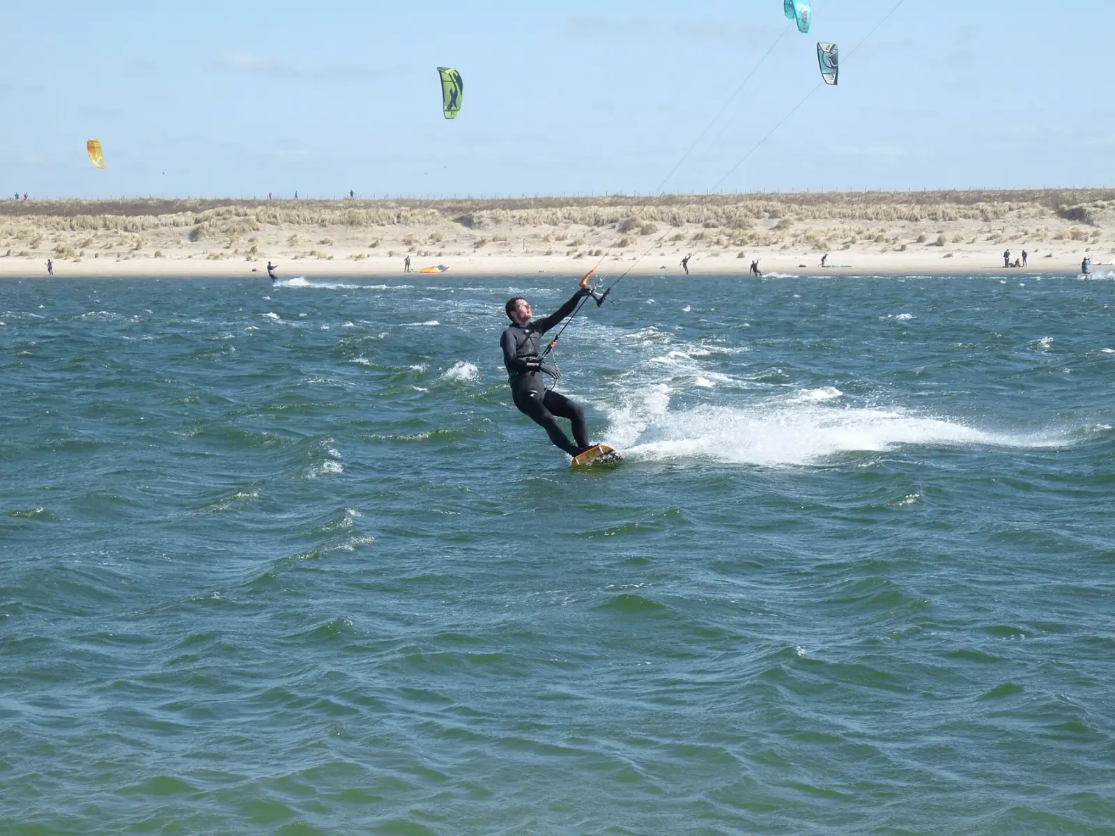 Een kiter op snelheid over kort, hobbelig water bij de Zandmotor, met de duinen erachter