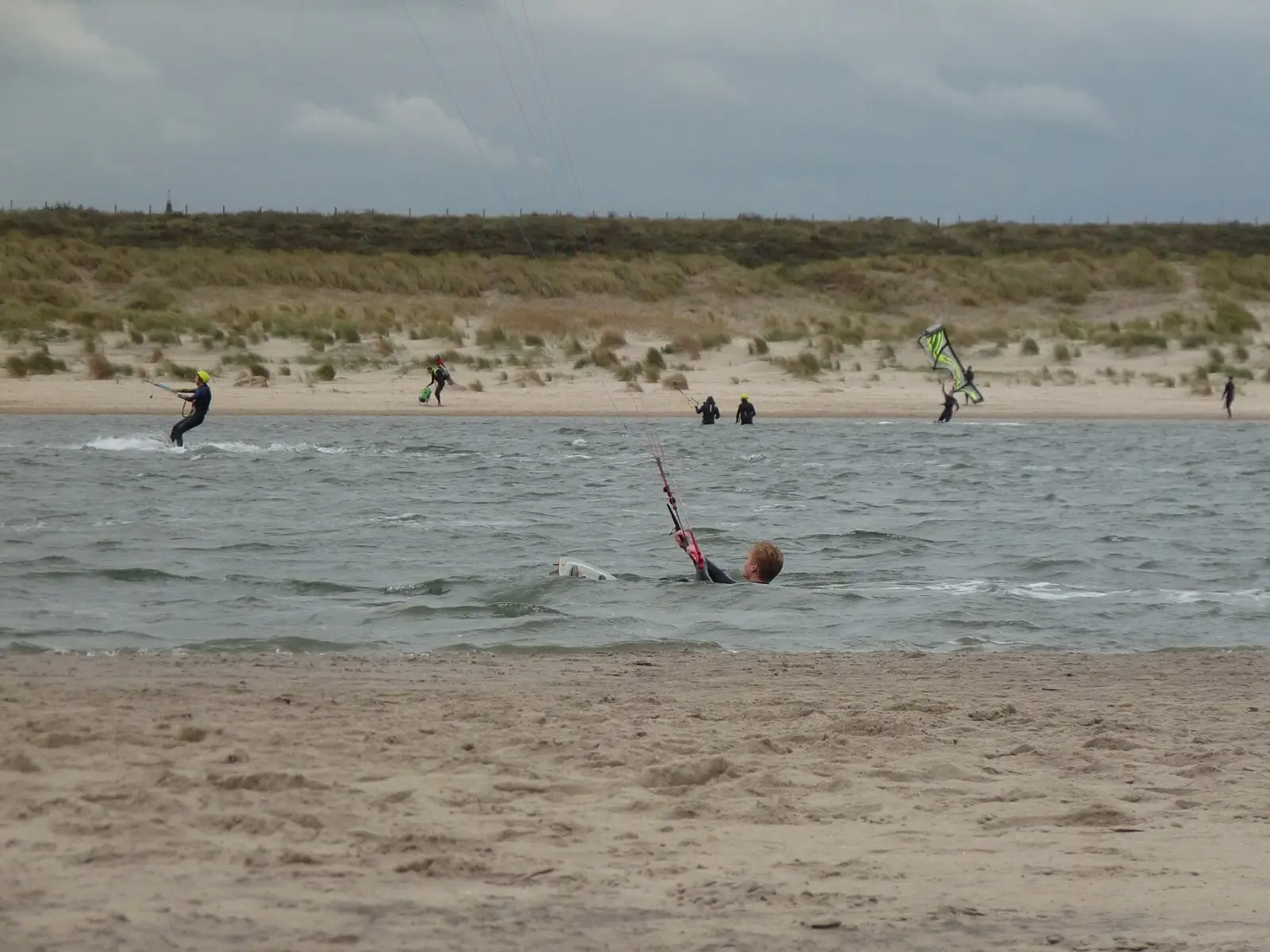 Mensen staan tot hun middel in ondiep water met kites vlak bij het strand